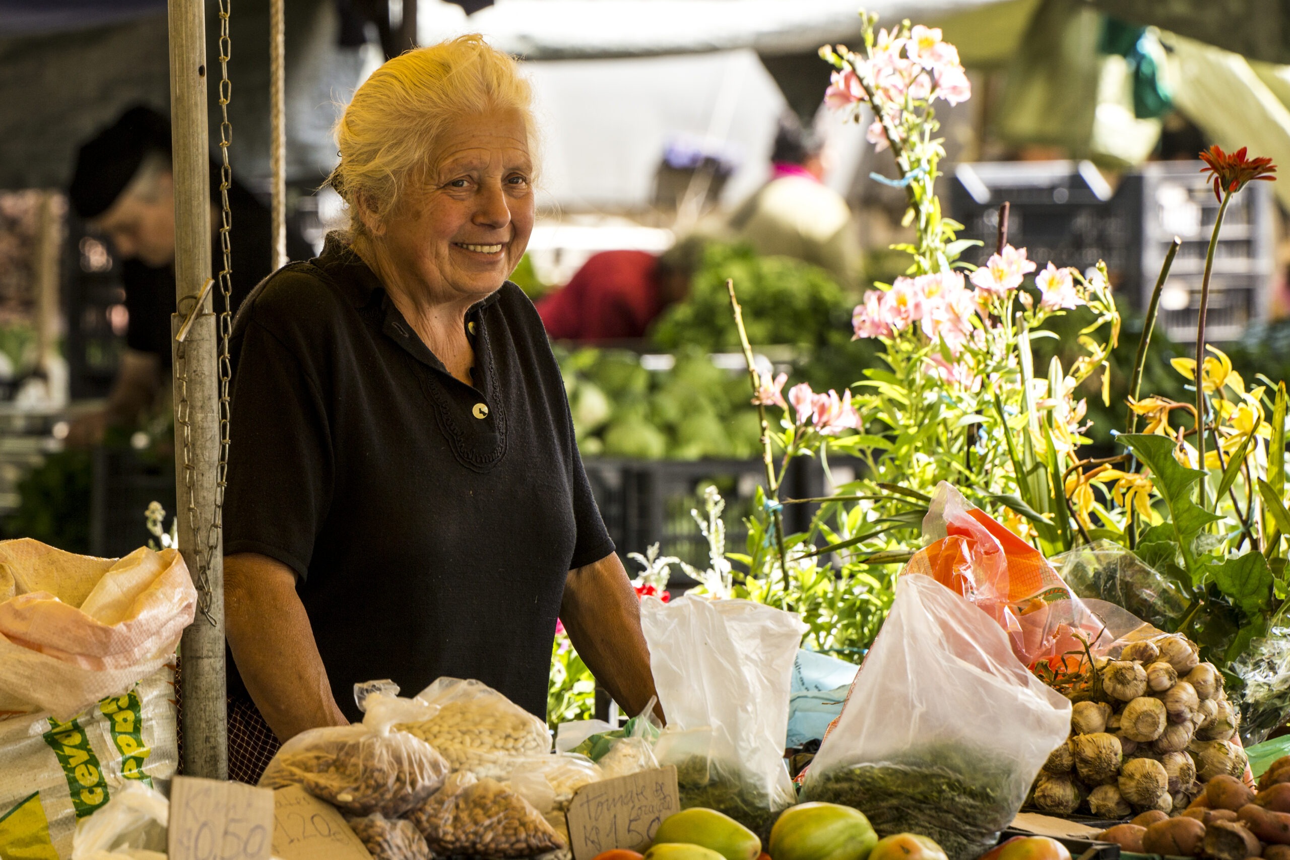 Smiling local vendor at famous Feira de Barcelos Thursday market, selling fresh vegetables, dried beans and other produce alongside colourful flowers